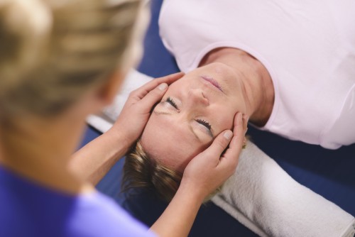 Alternative traditional medicine and massage, young spirit healer doing reiki treatment to old woman. Head and shoulders